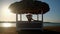 Woman sitting at Cabana with straw roof on a sandy beach on sunset