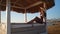 Woman sitting at Cabana with straw roof on a sandy beach on sunset