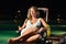 Woman is sitting on chair at poolside at night