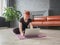 Woman sitting cross-legged on yoga mat and looking into laptop. Red hair girl choosing exercise online. Healthy