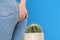 Woman sitting down on cactus against blue background, space for text. Hemorrhoid concept