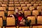 Woman sitting in empty theater hall with legs on backs of chairs