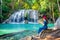 Woman sitting at Erawan waterfall in Thailand. Beautiful waterfall with emerald pool in nature.