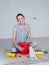 A woman sitting on the floor mixes glue in a red bucket for wallpapering in the apartment.