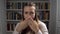 Woman sitting in front of bookshelf and closes her mouth with hands