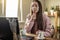 Woman is sitting in front of a computer screen and sniffing essential oil from a bottle to relax and restore energy