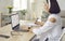 Woman sitting in front of laptop at home, studying online business course and taking notes