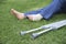 Woman sitting on the grass, feet, one of them with a bandage, and crutches