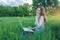 Woman sitting on a green meadow on the background of sunset with clouds. Working on laptop and talking on the phone.