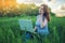 Woman sitting on a green meadow on the background of sunset with clouds. Working on laptop and talking on the phone.