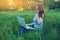 Woman sitting on a green meadow on the background of sunset with clouds. Working on laptop and talking on the phone.