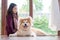 The woman sitting with her lovely brown Akita dog in the living room beside the windows. Outside the window is the garden. Looking