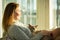 Woman sitting at home in a chair by the window stroking cat on her laps