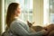 Woman sitting at home in a chair by the window stroking cat on her laps