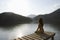 Woman Sitting On Lakeside Jetty At Dawn