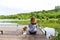 Woman sitting on the pier with her puppy and admiring the landscape