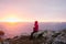 Woman sitting on the rocks watching the sunset in Martins Haven with St. Brides Bay in the background in Pembrokeshire, Wales, UK