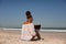 Woman sitting on sand and using laptop at beach in the sunshine