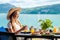 Woman sitting at table in cafe with sea view drinking orange juice