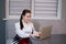 woman sitting by the table on couch in grey room - office and use laptop. big boss. important, confident women