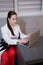 woman sitting by the table on couch in grey room - office and use laptop. big boss. important, confident women