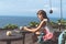 Woman sitting in a tropical restaurant with ocean view. Original place. Space for text. Bali island.