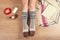 Woman sitting on the wooden floor with cup of coffee, phone, cookie and book. Close-up of female legs in warm socks with a deer vi
