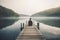 Woman sitting on a wooden pier on a lake in the misty morning. Generative AI