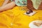 Woman sitting on the yellow cover. Closeup of wine glass, picnic basket with food and flower on the green grass