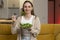 Woman is sitting on a yellow sofa enjoying a nutritious salad for lunch.