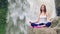 Woman sitting in yoga lotus pose on the edge next to Tegenungan Waterfall