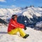 Woman skier enjoying the sun on the slopes of Les Sybelles ski domain, France, during a break, with snow-capped mountains.