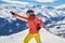 Woman skier smiling and posing at Les Sybelles ski domain, with Aiguilles d`Arves peaks in the background, on a sunny day.