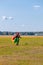 A woman skydiver walks across the field with a parachute.