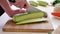 Woman slices courgette on a wooden cutting board on white table