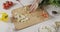 Woman slices green leek for salad preparation with a knife on cutting wooden board on a white kitchen table. Top view