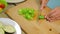 Woman slices green long chili pepper with a knife on a wooden board