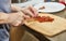 Woman slices sun-dried tomatoes on wooden board to make sun-dried tomato muffins