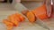 Woman is slicing fresh carrot on wooden cutting board