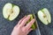 Woman slicing a green Granny Smith apple on a plastic man made faux gray granite cutting board, hands and chefs knife, apple halve