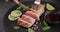 Woman slicing Grilled tuna steak on a black stone serving board with teriyaki soy sauce and pieces of lime