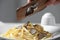 Woman slicing truffle onto fettuccine at table, closeup