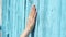 Woman slide hand against blue-colored wooden door in slow motion. Female hand touch surface of wood