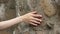 Woman sliding hand against old stone wall in slow motion. Female hand touching rough surface of rock