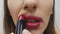 Woman smearing lipstick on the face. Close up of female incorrectly applying lipstick on lips against white background. Slow motio