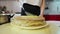 Woman smears cream on top of a cake which is on a round wooden spinning tray with a black spoon