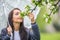 Woman smells tree flowers on during a spring rainy day in the nature, holding an umbrella