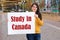 A woman smiles and holds a poster with the text Study in Canada