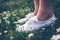 Woman in sneakers standing on meadow with flowers.