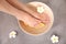 Woman soaking her feet in bowl with water, orange slices and flower on grey background, top view